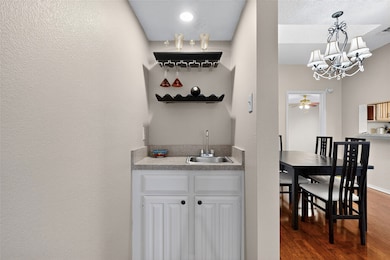 Indoor wet bar with open shelves, white cabinetry, wood-style flooring, a beautiful chandelier & decorative light fixtures
