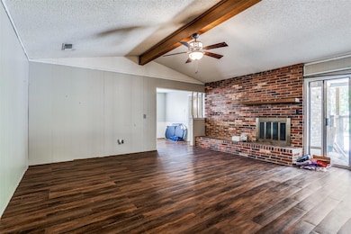 Unfurnished living room featuring lofted ceiling with beams, a brick fireplace, and dark hardwood / wood-style floors