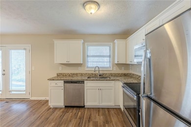 Kitchen featuring white cabinets, stainless steel appliances, a sink, and wood finished floors
