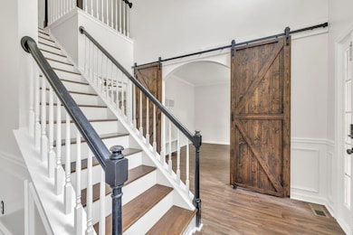 Stairway featuring a barn door, wood finished floors, and arched walkways