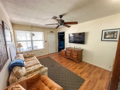 Living room featuring light wood-style floors, ceiling fan, a textured ceiling, and baseboards