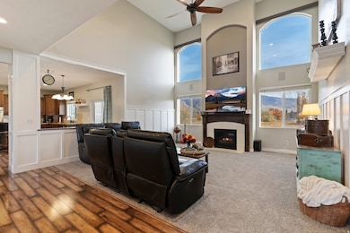 Carpeted living area with a ceiling fan, a towering ceiling, a tiled fireplace, a decorative wall, and a chandelier