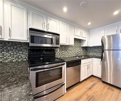 Kitchen with appliances with stainless steel finishes, white cabinetry, decorative backsplash, light wood-type flooring, and recessed lighting