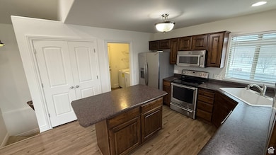 Kitchen with dark countertops, a kitchen island, stainless steel appliances, light wood-type flooring, and a sink