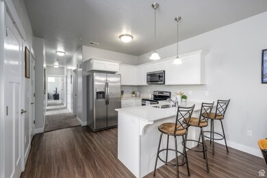 Kitchen with stainless steel appliances, white cabinetry, a breakfast bar area, a peninsula, and dark wood-style floors