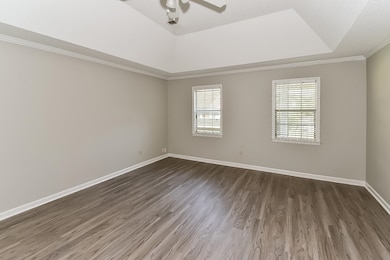 Empty room featuring a tray ceiling, wood finished floors, ornamental molding, and ceiling fan