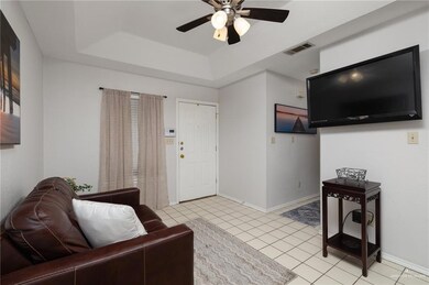 Living area with visible vents, baseboards, a tray ceiling, light tile patterned floors, and a ceiling fan