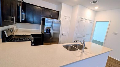 Kitchen featuring appliances with stainless steel finishes, a peninsula, dark wood finished floors, and light stone counters