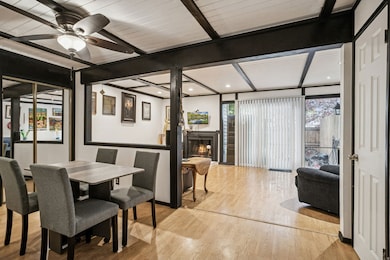 Dining space with wood finished floors, beam ceiling, a lit fireplace, floor to ceiling windows, and recessed lighting
