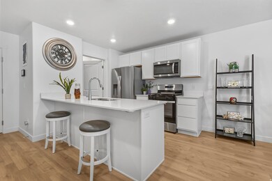 Kitchen featuring stainless steel appliances, a kitchen breakfast bar, white cabinetry, a peninsula, and light wood-style flooring