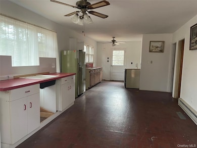Kitchen with white cabinets, freestanding refrigerator, ceiling fan, and baseboard heating
