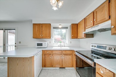 Kitchen with white appliances, under cabinet range hood, a peninsula, and plenty of natural light