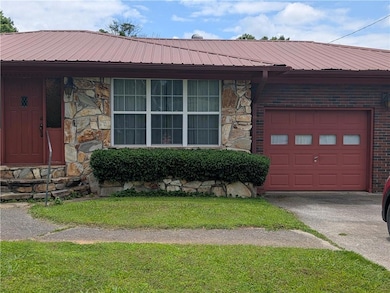 Ranch-style house with stone siding, concrete driveway, and metal roof