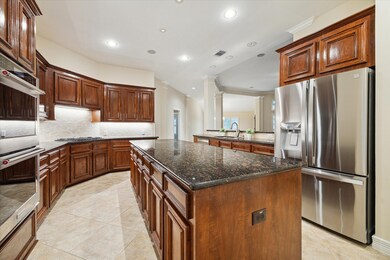 The kitchen features rich, dark wood cabinetry, granite countertops, modern appliances, a central island, and recessed lighting, creating a warm and inviting space for cooking and entertaining.