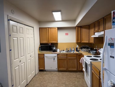 Kitchen with white appliances, brown cabinets, light tile patterned floors, light countertops, and under cabinet range hood