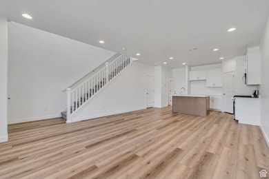 Unfurnished living room with light wood-type flooring, recessed lighting, and stairway