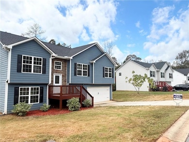 Raised ranch featuring a front yard, an attached garage, driveway, a wooden deck, and a shingled roof
