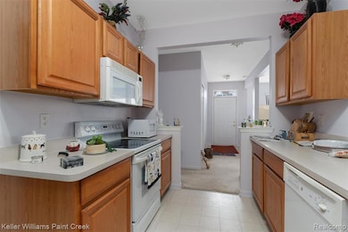 Kitchen with white appliances, light countertops, brown cabinets, and light colored carpet