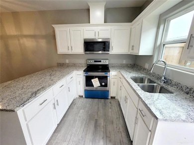 Kitchen featuring stainless steel appliances, white cabinets, light stone counters, light wood-style floors, and a peninsula