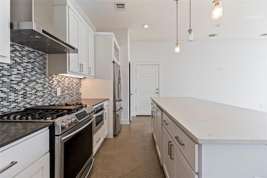 Kitchen featuring stainless steel appliances, white cabinetry, wall chimney exhaust hood, pendant lighting, and concrete flooring
