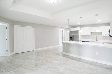 Kitchen with white cabinets, appliances with stainless steel finishes, hanging light fixtures, a tray ceiling, and light stone countertops