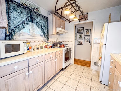 Kitchen featuring light countertops, white appliances, light tile patterned flooring, pendant lighting, and under cabinet range hood