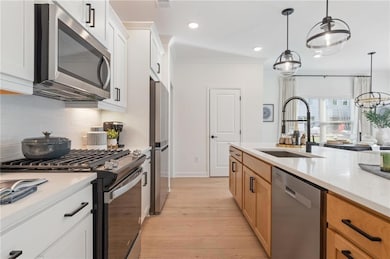 Kitchen with appliances with stainless steel finishes, a sink, decorative backsplash, light wood finished floors, and light countertops