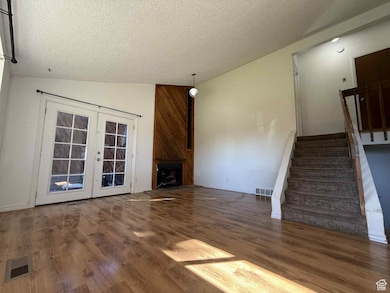 Unfurnished living room featuring dark wood finished floors, lofted ceiling, stairs, a textured ceiling, and french doors