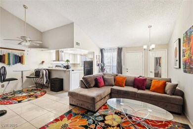 Living room featuring visible vents, a textured ceiling, ceiling fan with notable chandelier, light tile patterned floors, and vaulted ceiling