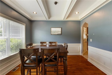 Dining space featuring arched walkways, beamed ceiling, wainscoting, crown molding, and wood finished floors