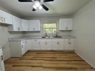 Kitchen with white cabinets, light countertops, light wood-style floors, and ceiling fan