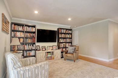 Living area featuring baseboards, crown molding, recessed lighting, wood finished floors, and bookshelves