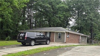 Ranch-style home with brick siding, driveway, fence, and view of wooded area