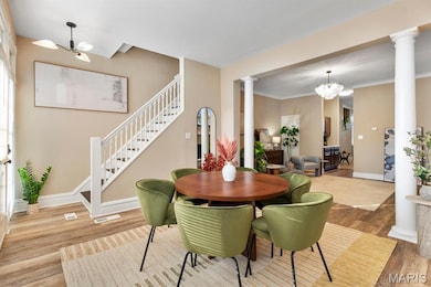Dining space featuring a chandelier, wood finished floors, stairs, crown molding, and ornate columns
