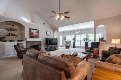 Living area featuring light colored carpet, a ceiling fan, a fireplace, and high vaulted ceiling