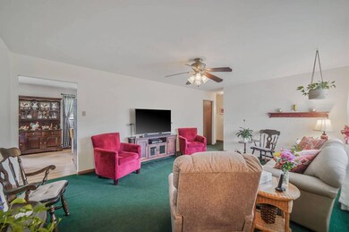 Carpeted living room with ceiling fan and baseboards