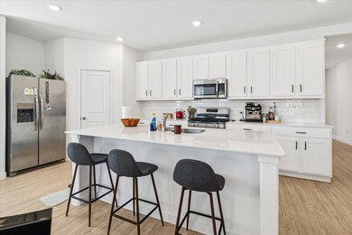 Kitchen with appliances with stainless steel finishes, white cabinetry, light wood-type flooring, recessed lighting, and a kitchen bar