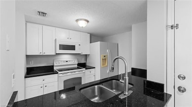 Kitchen featuring white appliances, a sink, a textured ceiling, white cabinetry, and dark stone counters