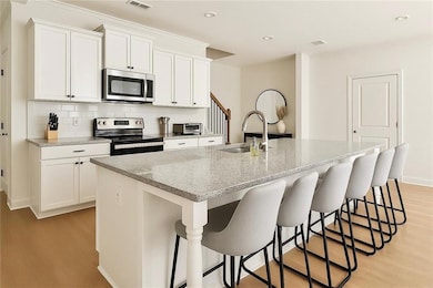 Kitchen featuring appliances with stainless steel finishes, a sink, light wood finished floors, an island with sink, and backsplash