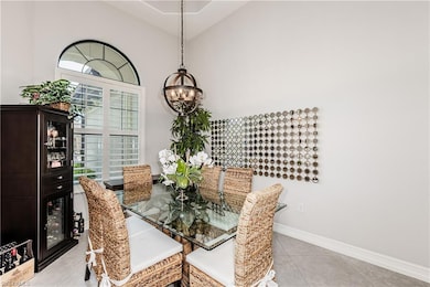 Dining area with a chandelier, light tile patterned floors, baseboards, and high vaulted ceiling