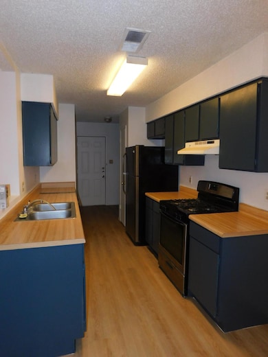 Kitchen with stove, light wood-style flooring, light countertops, a textured ceiling, and range hood