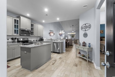 Kitchen with stainless steel appliances, a peninsula, a center island, light wood-type flooring, and light stone counters