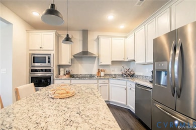 Kitchen with stainless steel appliances, light stone counters, wall chimney range hood, decorative light fixtures, and dark wood finished floors