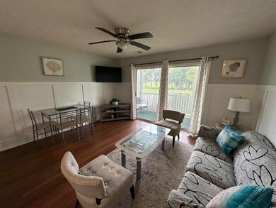 Living room featuring wainscoting, a decorative wall, a textured ceiling, wood finished floors, and a ceiling fan