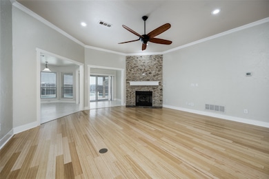 Unfurnished living room with crown molding, light wood-style floors, a ceiling fan, and a stone fireplace
