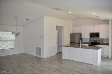 Kitchen featuring vaulted ceiling, white cabinetry, decorative backsplash, appliances with stainless steel finishes, and pendant lighting