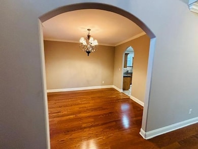 Unfurnished dining area featuring crown molding, arched walkways, a chandelier, wood finished floors, and baseboards