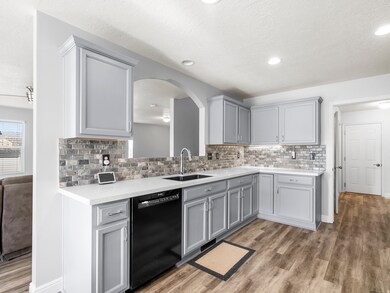 Kitchen featuring light wood-style flooring, gray cabinets, dishwasher, a textured ceiling, and decorative backsplash
