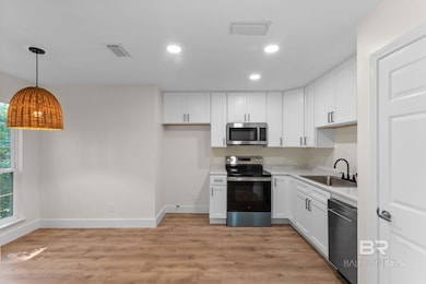 Kitchen featuring appliances with stainless steel finishes, white cabinetry, recessed lighting, light wood-type flooring, and hanging light fixtures