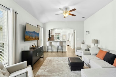 Living area featuring arched walkways, ceiling fan, light wood-type flooring, plenty of natural light, and lofted ceiling